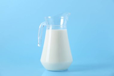 Açık mavi arkaplanda bir sürahi taze süt