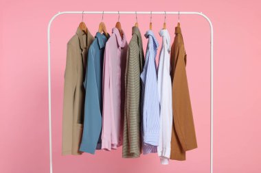 Rack with stylish clothes on wooden hangers against pink background clipart