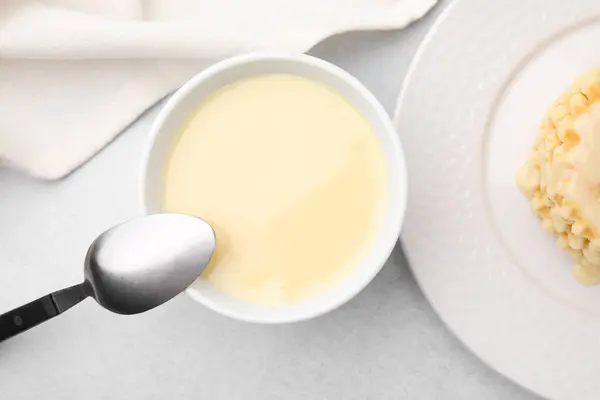 Tasty condensed milk in bowl and spoon on light grey table, flat lay