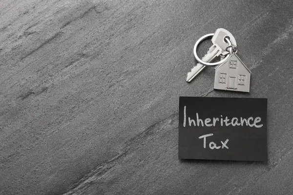 Inheritance Tax. Card and key with key chain in shape of house on grey table, top view. Space for text
