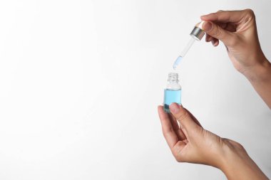 Beyaz arka planda bir şişe kozmetik serumu ve pipeti olan kadın, yakın plan. Metin için boşluk