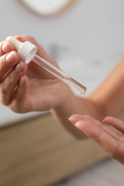 Kadın arka planda bulanık arka planda parmaklarına kozmetik serumu uyguluyor.