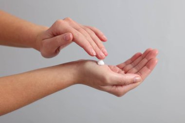 Woman applying cosmetic cream onto hand on light grey background, closeup