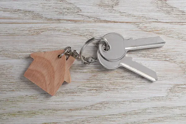 Keys with keychain in shape of house on light wooden table, top view