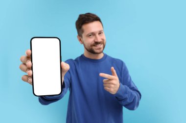 Akıllı telefonu elinde gösteren yakışıklı bir adam ve açık mavi arka planda ona işaret ediyor, seçici odaklanma. Tasarım için model