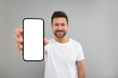 Açık gri arka planda akıllı telefon gösteren yakışıklı bir adam, seçici bir odak noktası. Tasarım için model