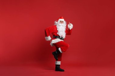 Mutlu noeller. Noel Baba kırmızı arka planda dans ediyor