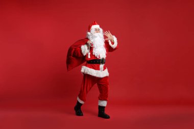 Kırmızı arka planda duran bir çanta dolusu Noel Baba.