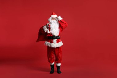 Kırmızı arka planda duran bir çanta dolusu Noel Baba.