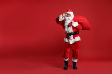 Kırmızı arka planda duran bir çanta dolusu Noel Baba, mesaj için yer