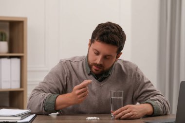 Depresyonda olan bir adamın elinde bir bardak su ve antidepresan haplar var.