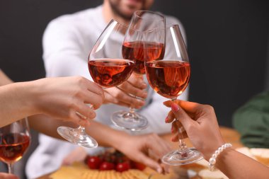 İnsanlar kadehlerini ahşap masanın üstünde gül şarabıyla tokuşturuyor.