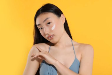 Yüzünde turuncu arka planda güneş kremi olan güzel genç bir kadın.