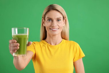 Yeşil arka planda bir bardak lezzetli kereviz suyu olan kadın.
