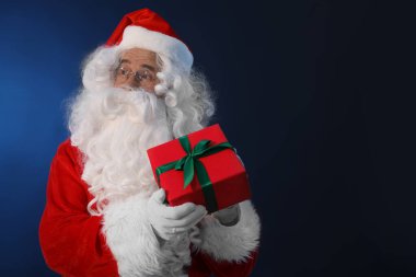 Koyu mavi arka planda Noel hediyesi olan Noel Baba. Metin için boşluk