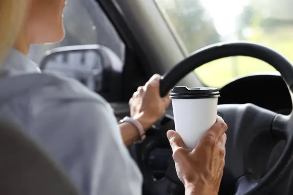 Coffee to go. Woman with paper cup of drink driving her car, closeup