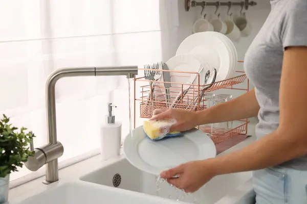 Woman washing plate at sink in kitchen, closeup