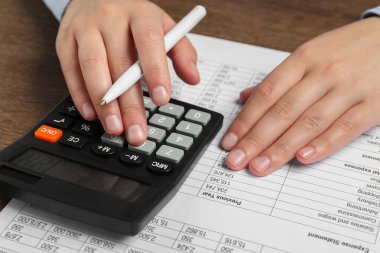 Tahta masadaki hesap makinesini kullanarak veri ile çalışan kadın, yakın plan