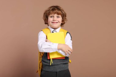 Sırt çantası ve kahverengi arka plan kitapları olan mutlu okul çocuğu.