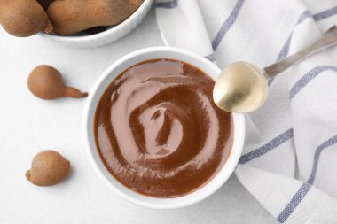 Bir kase demirhindi sosu, kaşık ve taze kapsüller ışık masasında.