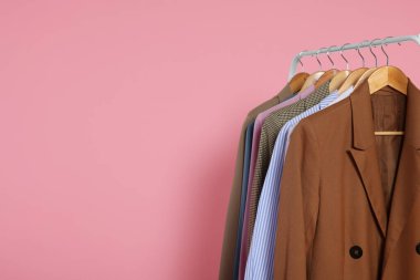 Ahşap askılarda pembe arka planda şık kıyafetler, metin için boşluk