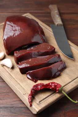 Biber, sarımsak ve bıçakla kesilmiş çiğ sığır ciğeri, ahşap masa, yakın plan