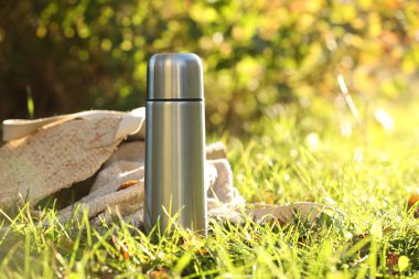 Metal thermos and bag with blanket on green grass outdoors, space for text clipart