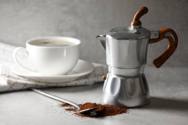 Ground Coffee, moka pot ve bardakla açık gri masada içki.