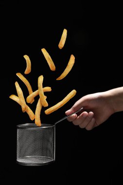 Patates kızartması siyah arka plandaki kadının tuttuğu metal sepete düşüyor.