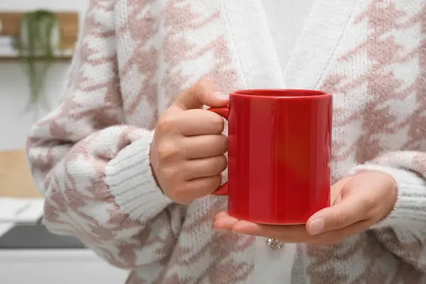 Woman holding red mug at home, closeup. Mockup for design