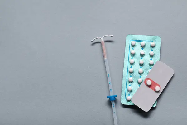 Birth control pills and intrauterine device on light grey background, flat lay and space for text. Choosing method of contraception