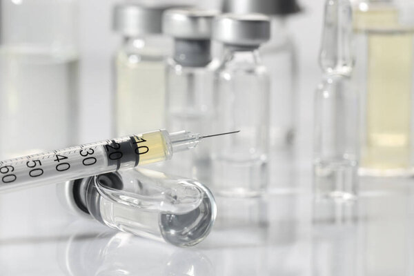 Glass vial and syringe with medication on white table, closeup. Space for text
