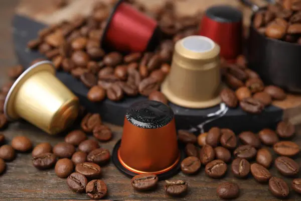 Coffee capsules and beans on wooden table, closeup
