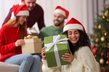 Arkadaşlar arasında Noel kutlaması. Evde hediye kutusu olan mutlu genç bir kadın, seçici bir odak noktası var.