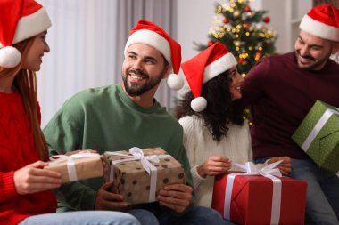 Noel kutlaması. Noel Baba şapkalı mutlu arkadaşlar evde hediye alışverişi yapıyorlar.