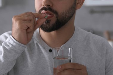 Bir bardak suyu olan bir adam bulanık arka planda antidepresan hapı alıyor.
