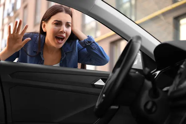 Automobile lockout, key forgotten inside. Emotional woman looking through car window