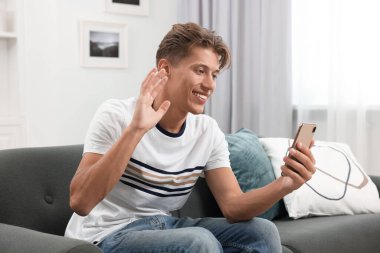 Mutlu genç adam akıllı telefondan kapalı koltukta görüntülü sohbet ediyor.