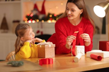 Noel hediyelerini paketliyorum. Anne ve küçük kızı evde kurdeleyle hediye kutusunu dekore ediyorlar.