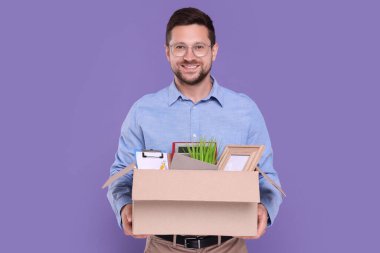 Mor arka planda kişisel eşyaları olan mutlu, işsiz bir adam.