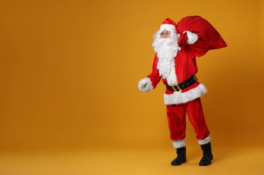 Noel Baba turuncu arka planda Noel hediyeleriyle dolu bir çanta, mesaj için boşluk