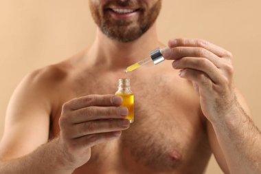 Bej arka planda kozmetik serumlu gülümseyen adam, seçici odaklanma
