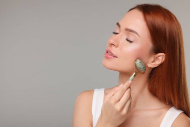 Genç bir kadın yüzüne gri arka planda yeşil bir silindirle masaj yapıyor. Mesaj için yer var.