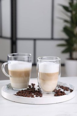 Aromatik latte macchiato ve kahve çekirdekleri beyaz mermer masada bulanık arka planda.