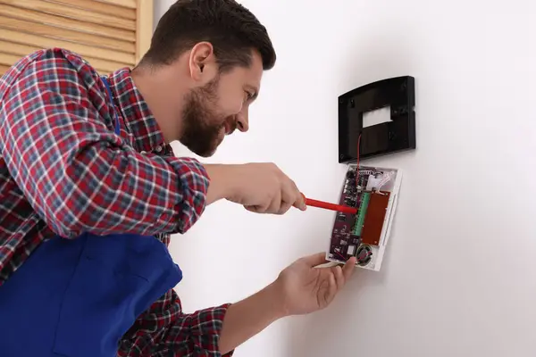 Technician installing home security alarm system on white wall indoors