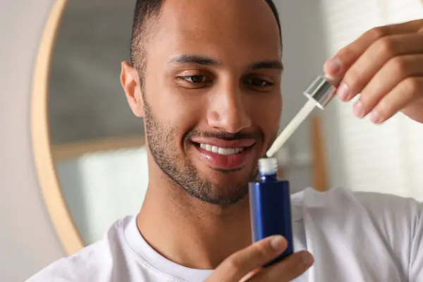 stock image Handsome man with cosmetic serum in hands indoors