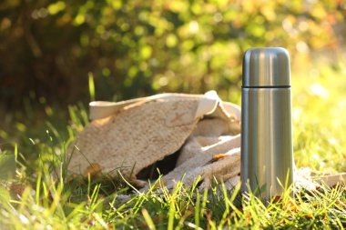 Metal thermos and bag with blanket on green grass outdoors clipart