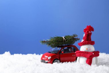 Tatlı dekoratif kardan adam ve köknar ağacı dalları olan oyuncak araba. Yapay kar üzerinde açık mavi arkaplan, metin için boşluk.