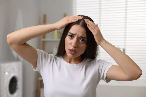 Emotional woman examining her hair and scalp in bathroom. Dandruff problem