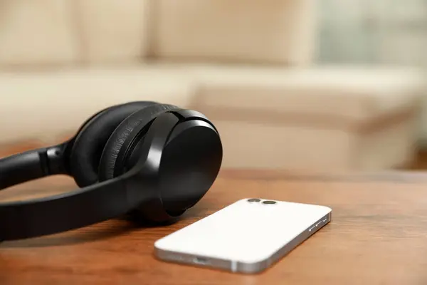 Modern wireless headphones and smartphone on wooden table indoors, closeup